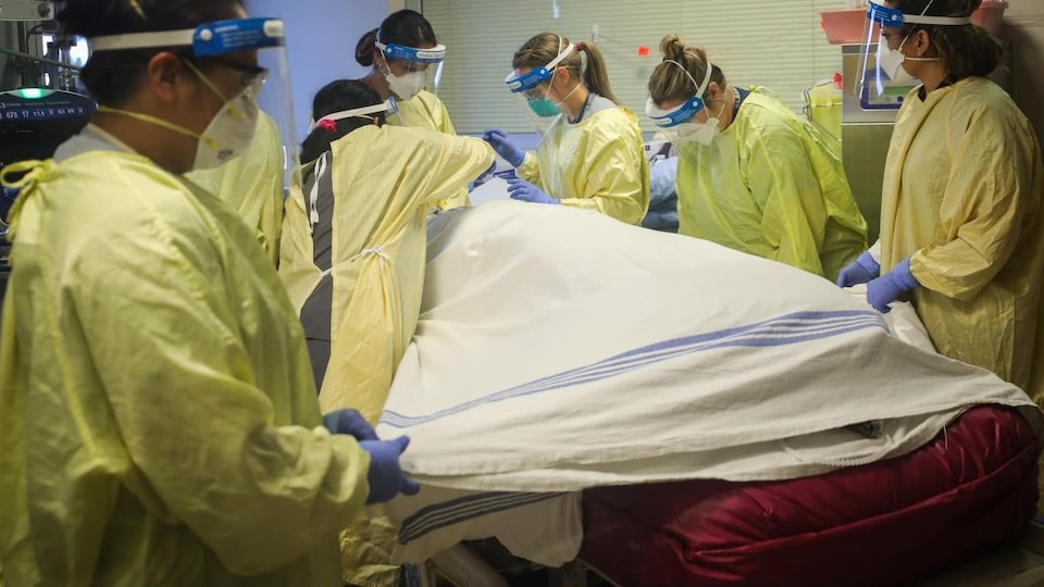 Du personnel hospitalier autour d'un lit où un patient est allongé recouvert d'un drap.