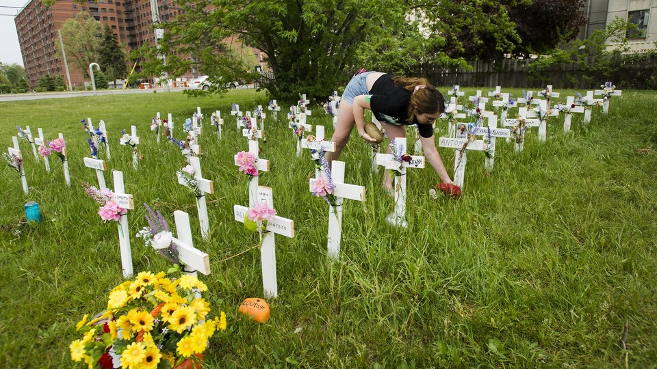 Une femme place une roche près de chacune des croix représentant une soixantaine de personnes qui sont mortes de la COVID-19 dans une résidence ontarienne.