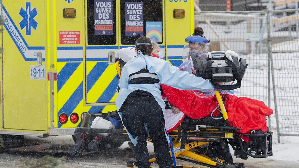 Deux personnes poussent une civière sur laquelle se trouve une patiente, près d'une ambulance.