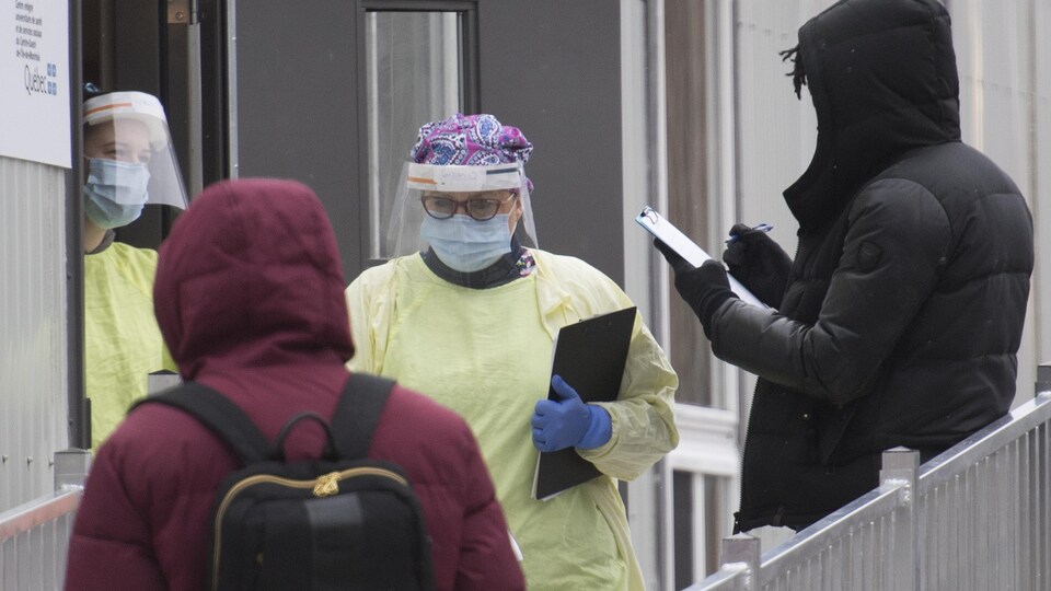 Deux travailleurs revêtus d'équipement de protection individuelle parlent à deux personnes à l'extérieur d'un bâtiment.