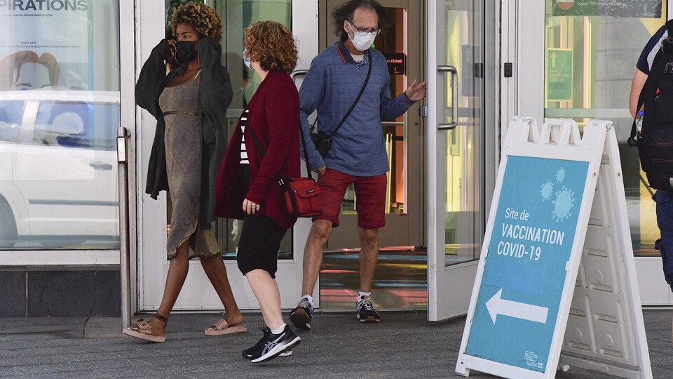 Un homme et deux femmes portant un masque de protection près d’un centre de vaccination à Montréal.