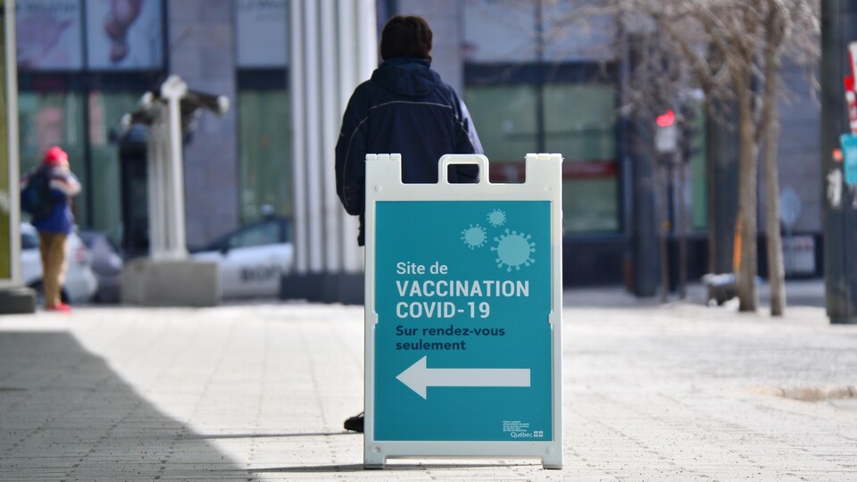 Une personne se tient de dos devant une pancarte indiquant une clinique de vaccination.