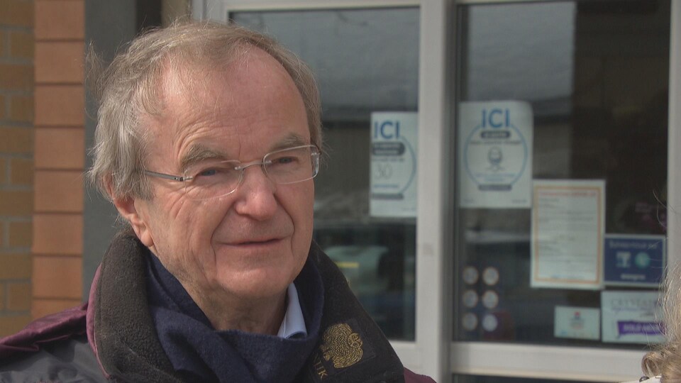 A man is standing outside a medical clinic, wearing a winter coat.