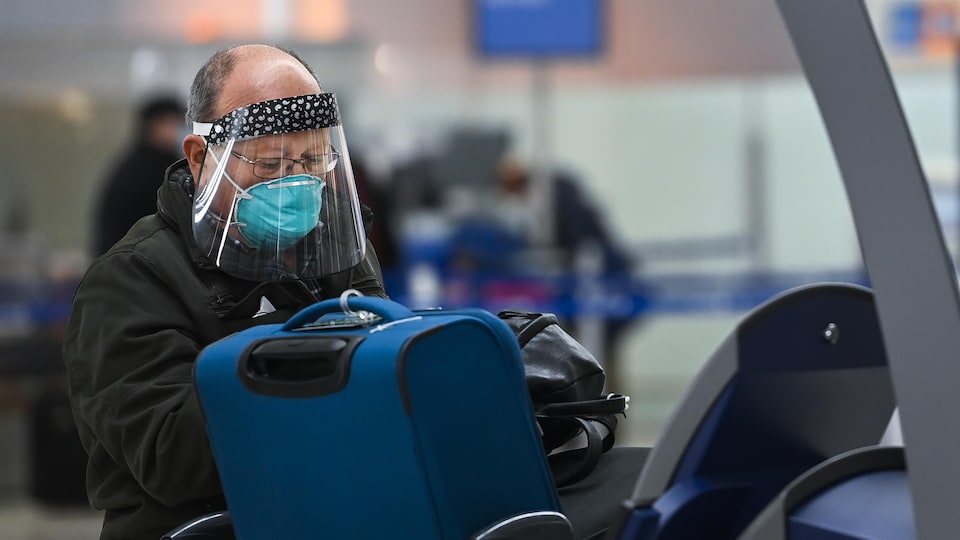Un voyageur portant un masque et une visière enregistre ses valises à l'aéroport Pearson.