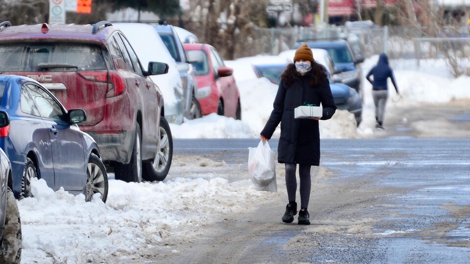 Une femme masquée marche dans la rue avec un paquet dans les mains.
