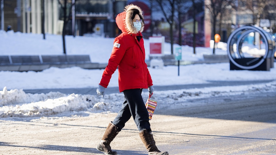 Une femme marche dans la rue avec un masque et des bottes.
