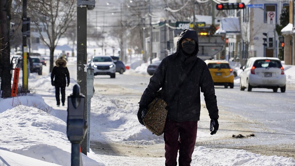 Une personne marche dans la rue en hiver, avec un masque au visage.