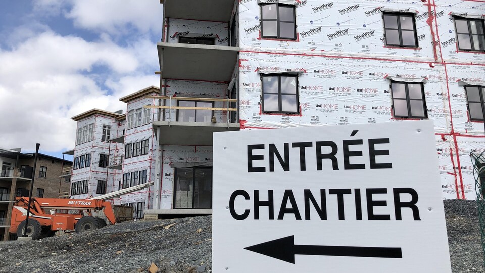 Construction d'un immeuble de logements où l'on voit en premier plan une pancarte indiquant « entrée chantier ».