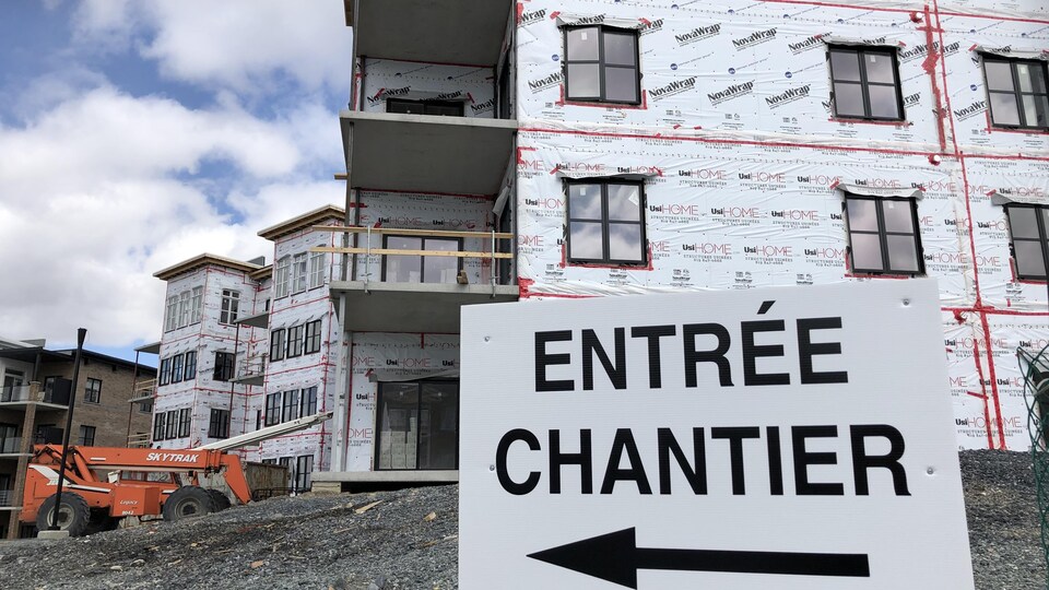 Construction d'un immeuble de logements où l'on voit en premier plan une pancarte indiquant « entrée chantier ». 