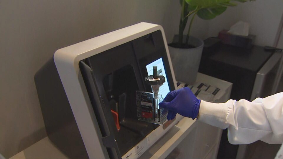 Une technicienne place un échantillon de salive dans un appareil.