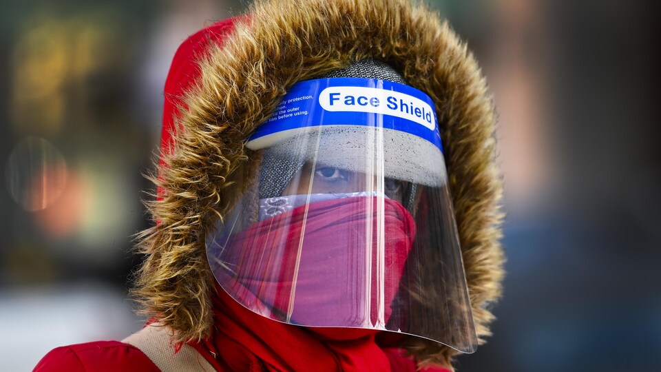 Une femme emmitouflée dans son capuchon avec un masque, un foulard et une visière.