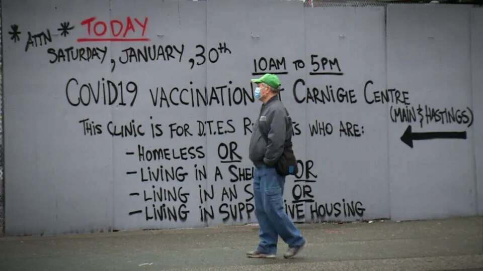 Un homme passant devant un mur où l'on a peint une invitation pour la clinique de vaccination. 