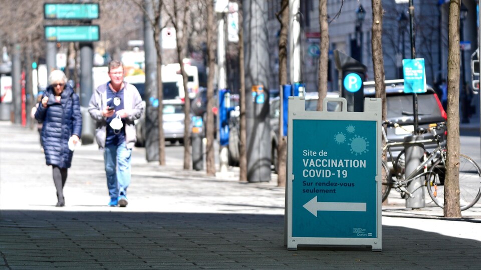 Des gens passent près d'une affiche indiquant un centre de vaccination.