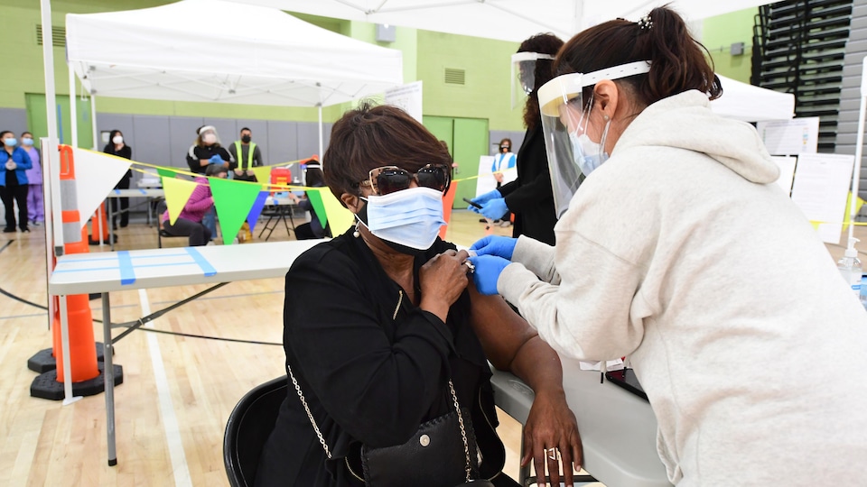 La femme, qui porte deux masques l'un sur l'autre et des lunettes de soleil, se fait vacciner.