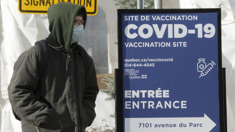 Un homme se tient près d'une pancarte qui annonce la présence d'un centre de vaccination.