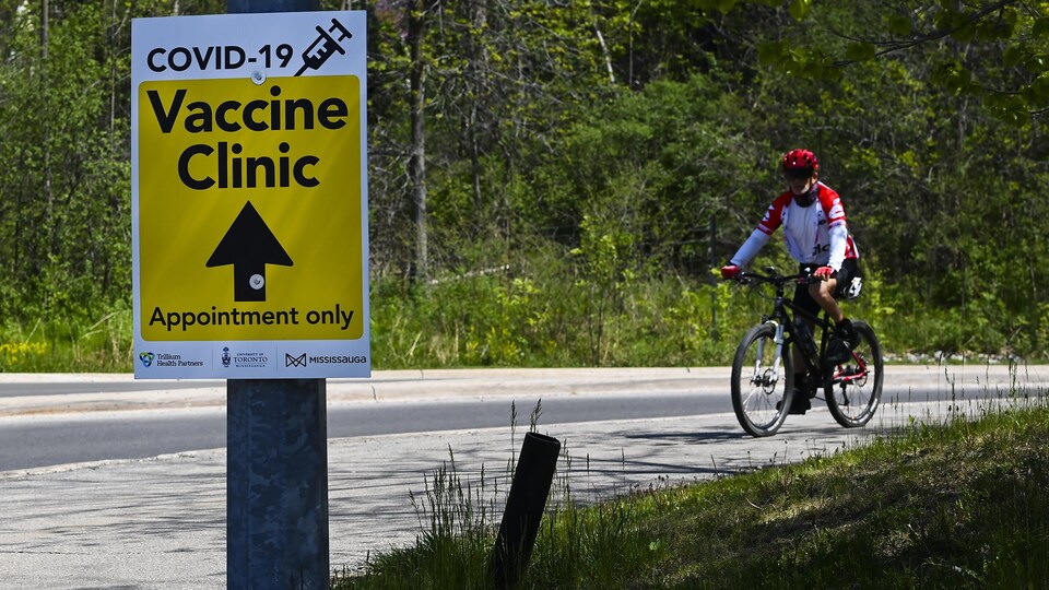Une personne passe à bicyclette devant la pancarte d'un centre de vaccination contre la COVID-19 au campus Mississauga de l'Université de Toronto.