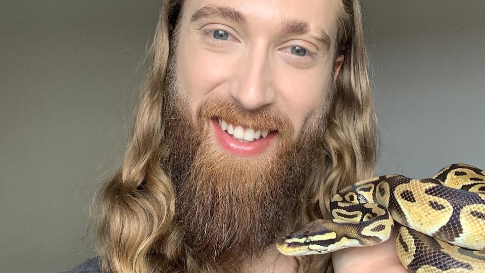 Un homme tient un serpent dans sa main à la hauteur de son visage.