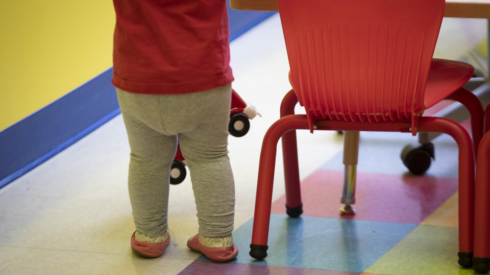 Une fillette se tient debout à côté d'une petite chaise pour enfant, un camion de plastique dans les mains.