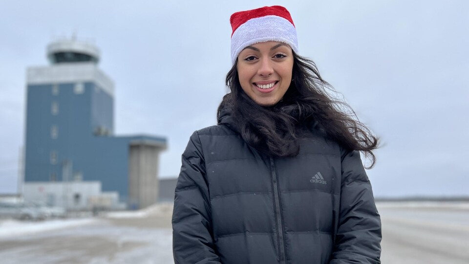 Une femme avec une tuque de Noël se tient sur une piste d'aéroport.