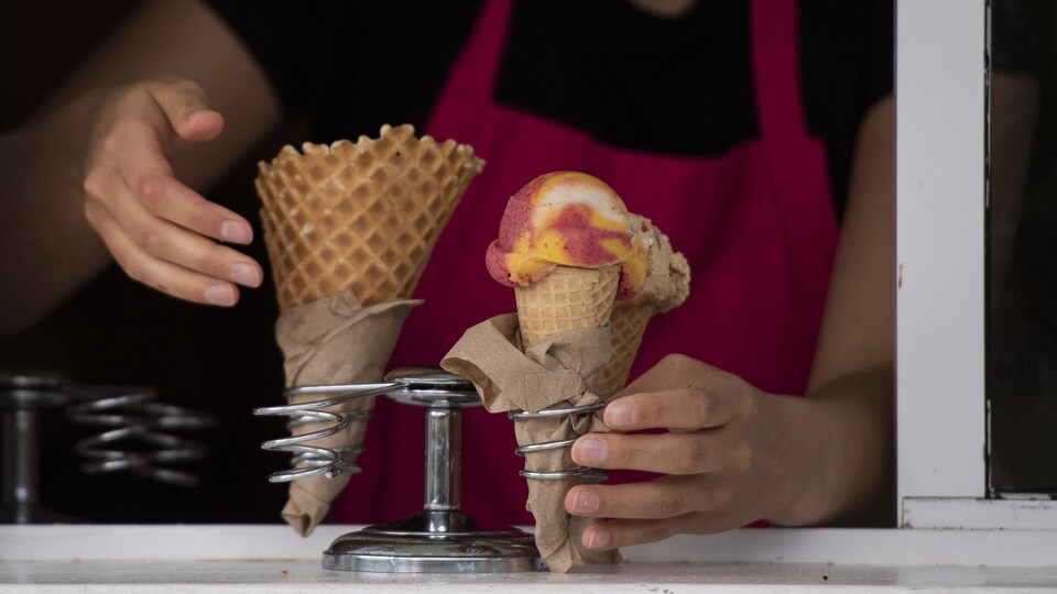 Une employée place des cornets de crème glacée dans un support extérieur.