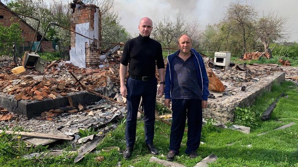 Yurii Bilous and a Ukrainian in front of the ruins of a house.