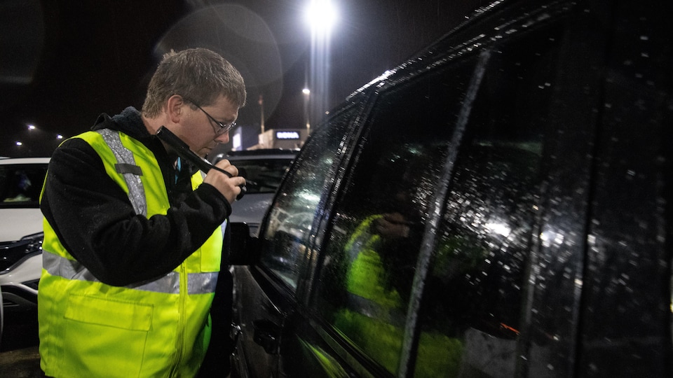 Un homme vérifie l'intérieur d'une voiture lors d'une patrouille, le soir.