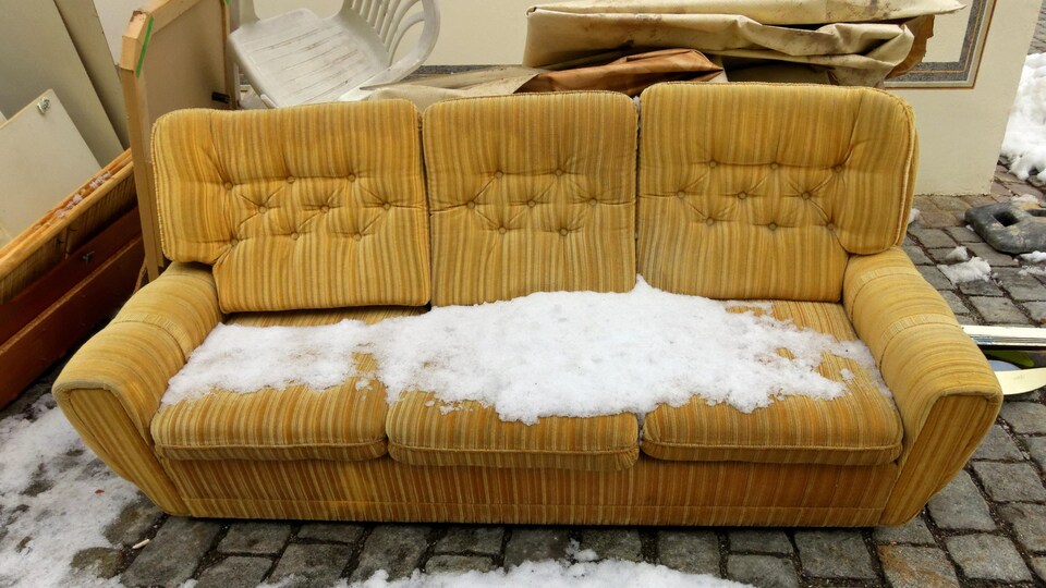 Un divan défraîchi partiellement couvert de neige, abandonné sur le trottoir.