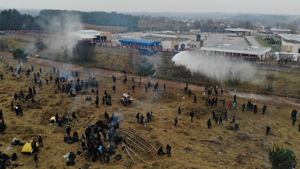 Des migrants font face aux tirs de gaz lacrymogène près d'une clôture à la frontière de la Pologne et du Bélarus.