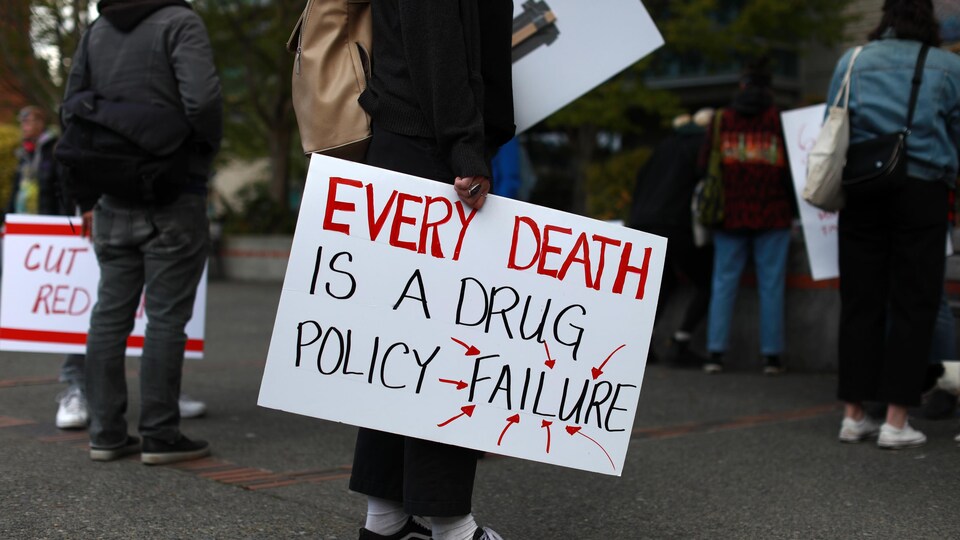 Une personne tient une affiche sur laquelle est écrit, en anglais, que « chaque mort est un échec des politiques sur les drogues ».