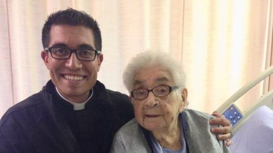 Le père Cristino Bouvette avec sa grand-mère sur un lit d'hôpital, en 2014