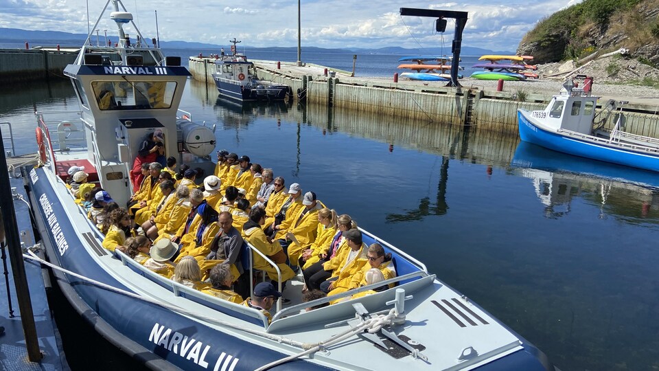 Une quarantaine de personnes sont assises dans un bateau amarré dans un petit port.