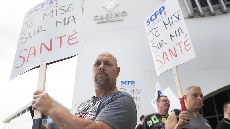 Des croupiers du Casino de Montréal manifestent avec des pancartes à la main.
