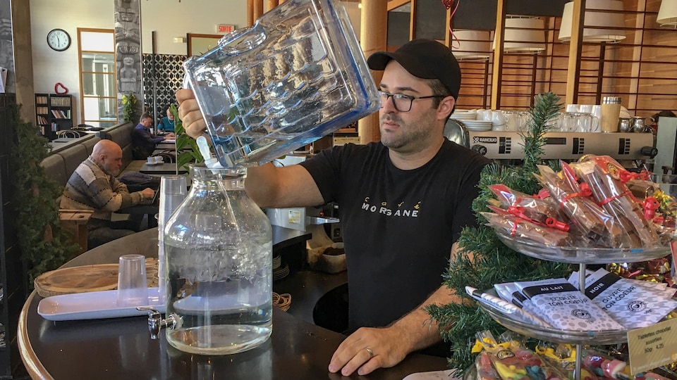 Un employé d'un café de Shawinigan verse de l'eau dans une distributrice.