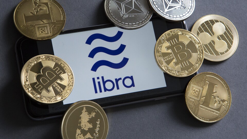 Téléphone avec le logo de Libra, entouré de pièces de monnaie or et argent.