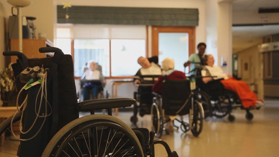 In one room, four residents in wheelchairs and a nurse. 