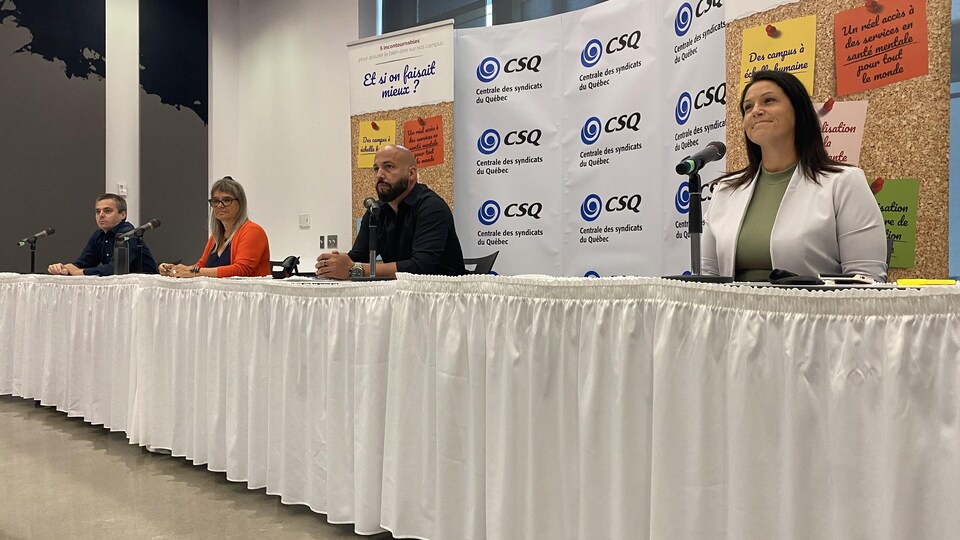 Deux hommes et deux femmes assis à une table derrière des microphones lors d'une conférence de presse.
