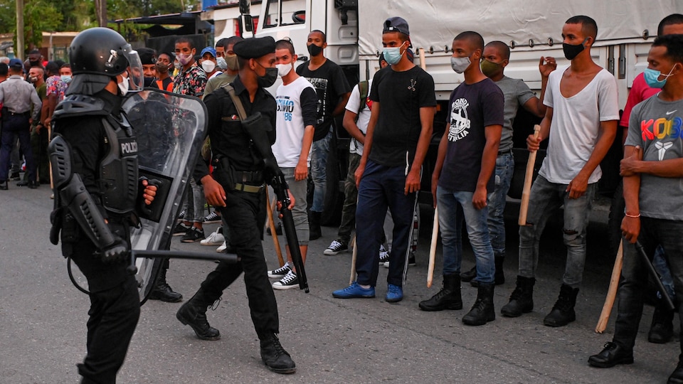 Des policiers lourdement armés devant des manifestants qui tiennent des bâtons.