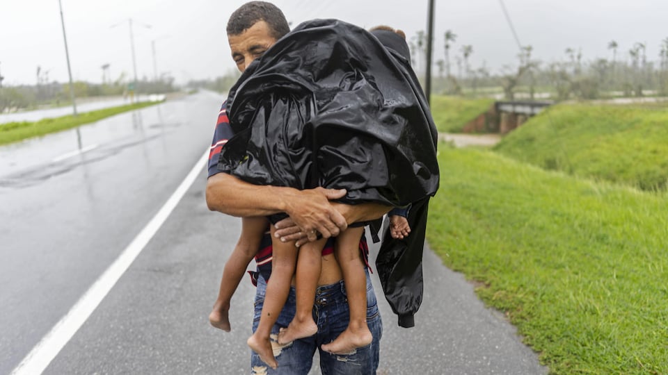 Un homme transporte deux enfants sous la pluie.