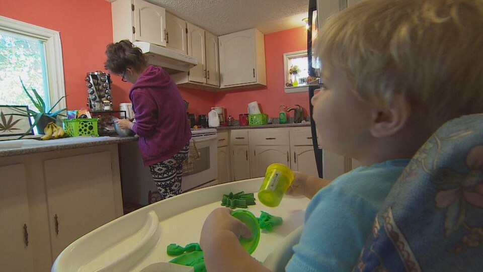 Une femme cuisine avec du cannabis chez elle avec son enfant qui l'observe, dans sa chaise haute.