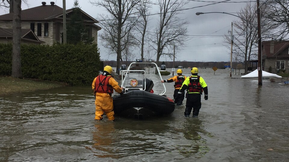 Des pompiers avec un bateau dans une rue inondée.