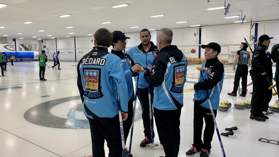 Les cinq membres de l'équipe Bédard discutent pendant que d'autres joueurs circulent sur la glace de curling.