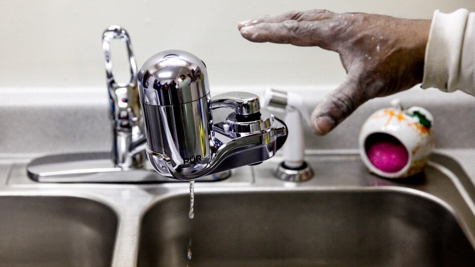 Une main s'apprête à ouvrir un robinet.