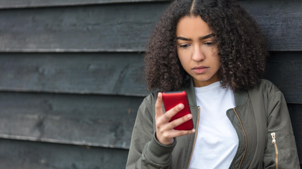Une adolescent regarde son téléphone cellulaire d'un air triste.