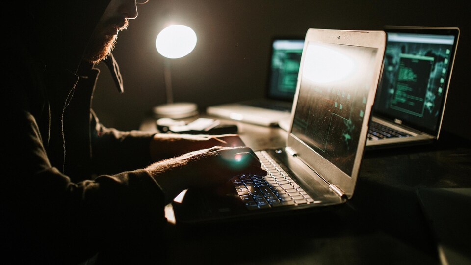 Un pirate informatique à l'œuvre dans une pièce sombre.