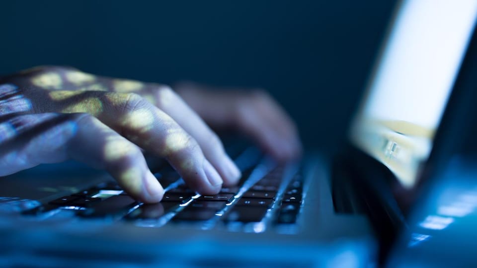 Un homme pose les mains sur le clavier d'un ordinateur portable dans l'obscurité.