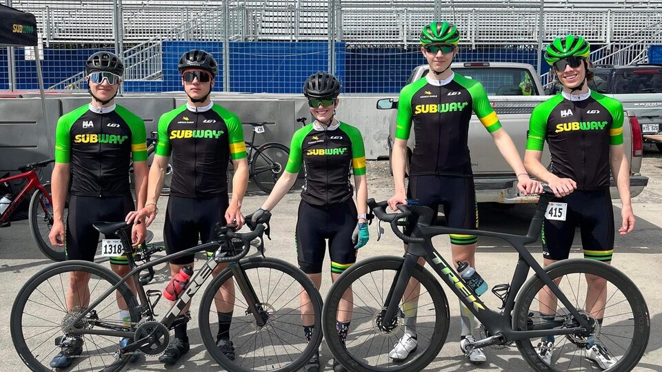 Cinq jeunes cyclistes, en uniforme Subway, prennent la pose pour la caméra avec deux vélos.