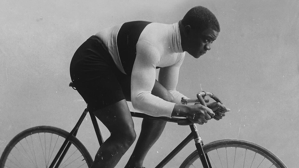 Sur cette photo d'archives, on voit le cycliste Major Taylor sur son vélo, de profil, prenant la pose comme s'il était en action.