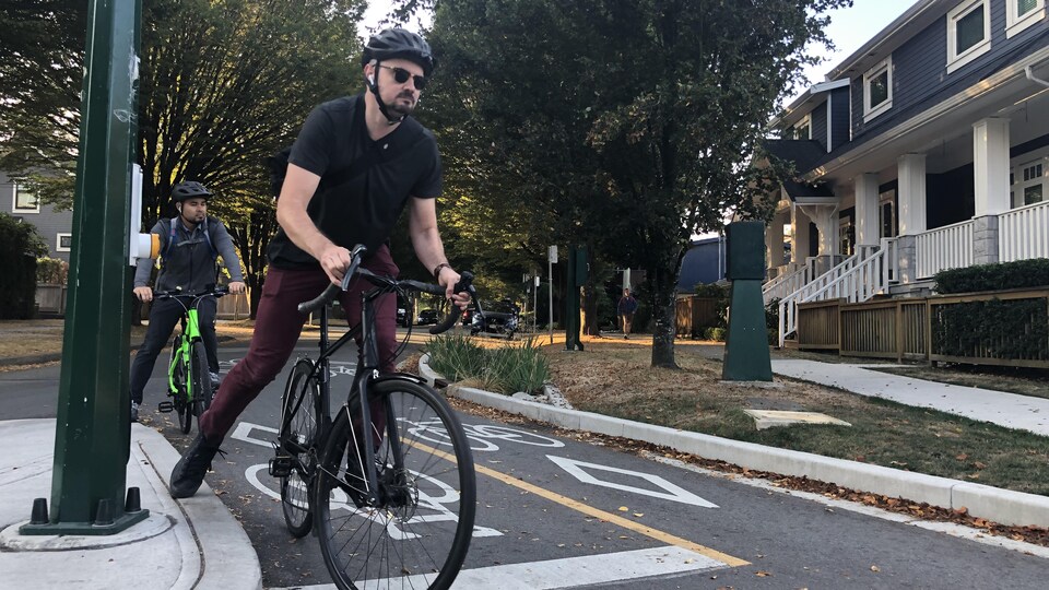 Deux cyclistes sur une piste cyclable dans un quartier résidentiel attendent de traverser à une intersection.