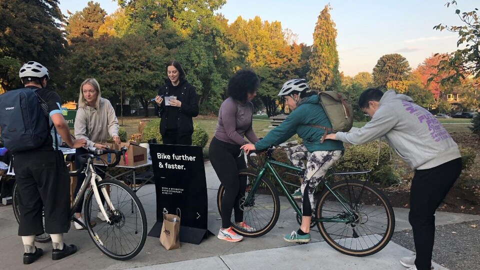Des cyclistes sont arrêtés à un kiosque où des bénévoles servent du café et d'autres font des ajustements de vélos.