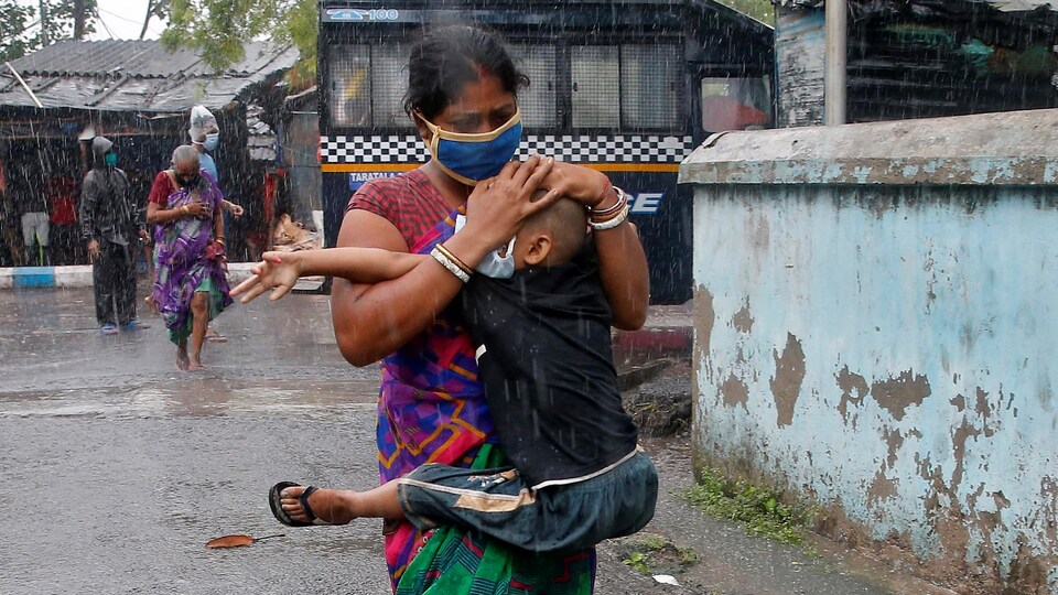 Une Indienne masquée tenant un garçon dans ses bras tente de lui protéger la tête d'une forte pluie avec ses mains.